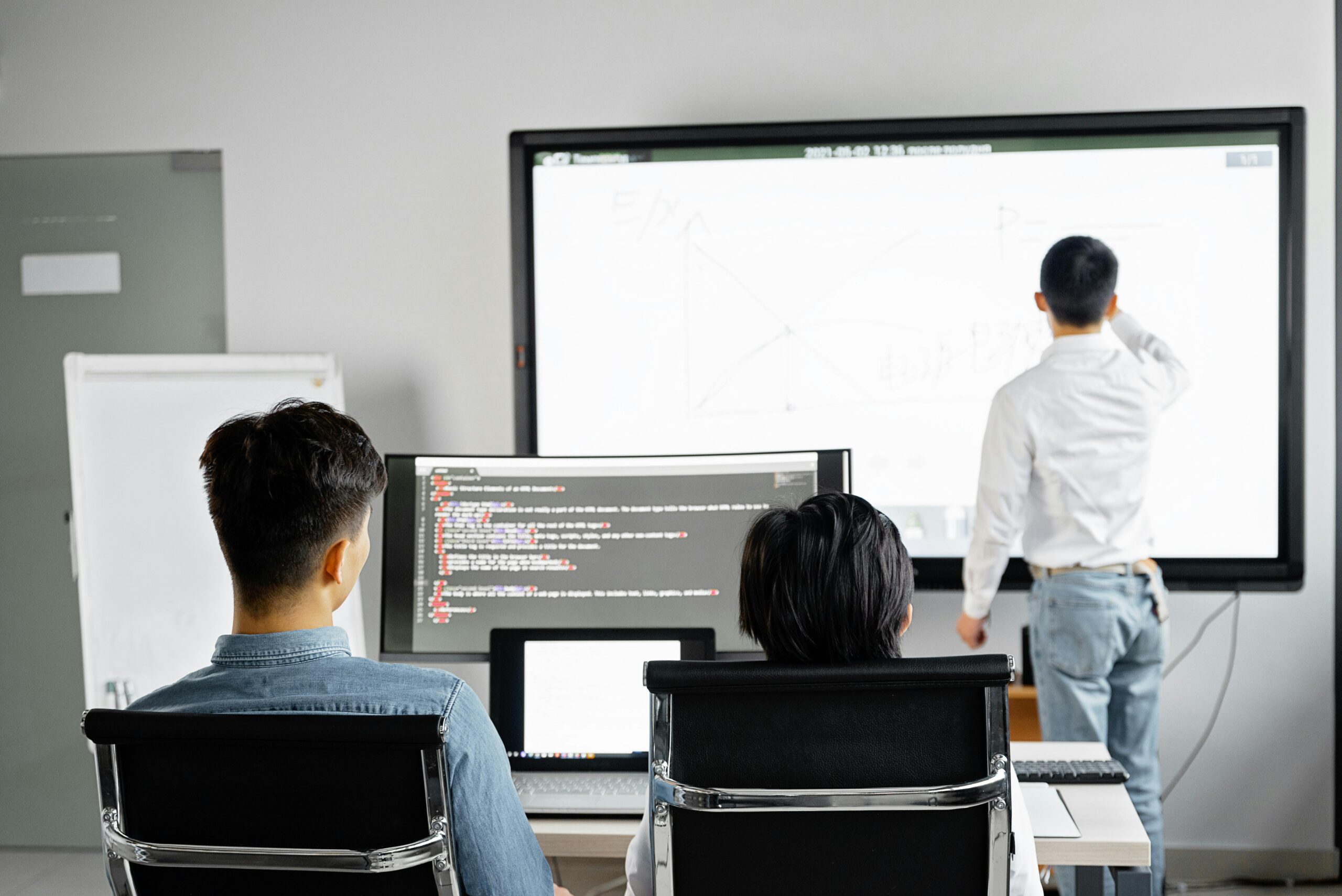 People attending a digital growth workshop, with one individual presenting at a large screen displaying visuals, while others follow along on computer monitors.